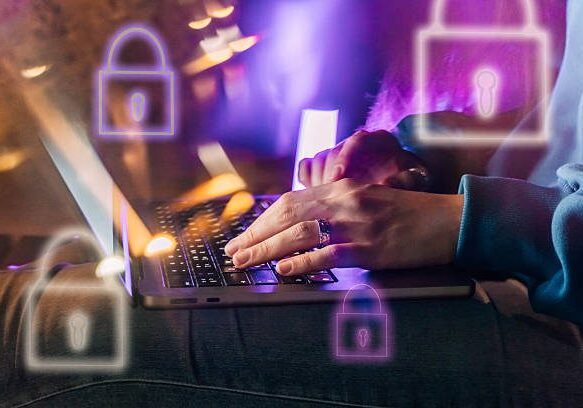 Female hands typing on a laptop in neon light. A lock as a symbol of cybersecurity on a foreground.